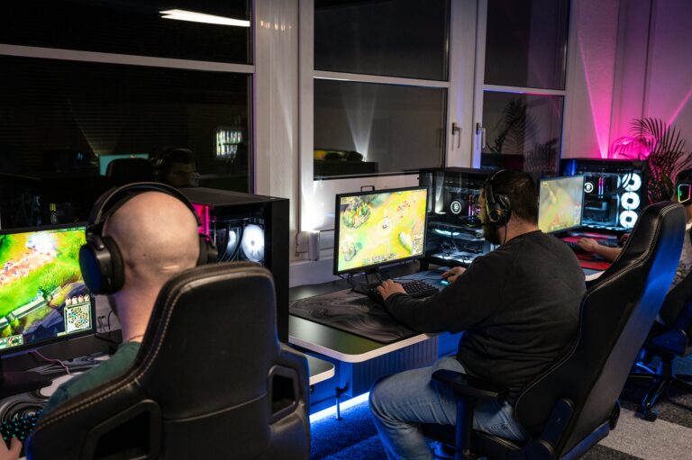 Duas pessoas sentadas em cadeiras gamer em frente a um computador, concentradas e jogando um jogo.