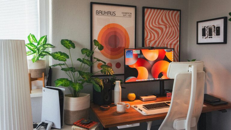 Um cantinho de estudos montado em um quarto, decorado com quadros laranjas na parede.