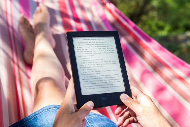 Pessoa relaxada aproveitando o dia ao ar livre enquanto realiza uma leitura confortável em seu leitor de livro digital em um jardim iluminado.